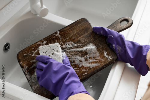 Obraz na płótnie Hands in purple rubber gloves washing a wooden cutting board with a sponge and s