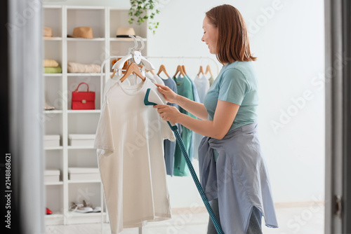 Canvastavla Young woman steaming a white t-shirt on a hanger in a modern home closet with or