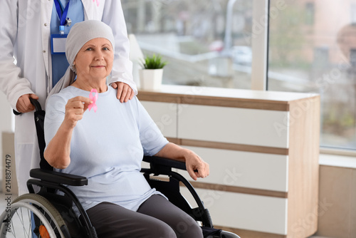 Senior woman in wheelchair after chemotherapy with pink ribbon and doctor at ...
