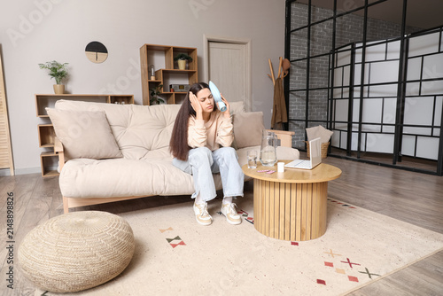 Young woman suffering from headache with heating pad at home