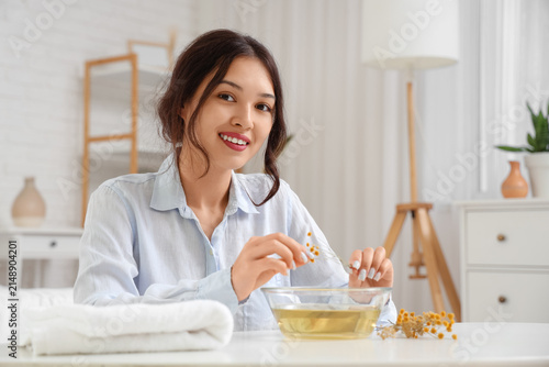 Young Asian woman preparing steam inhalation with herbs at table in bedroom