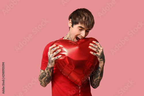 Funny young man with heart-shaped air balloon on pink background