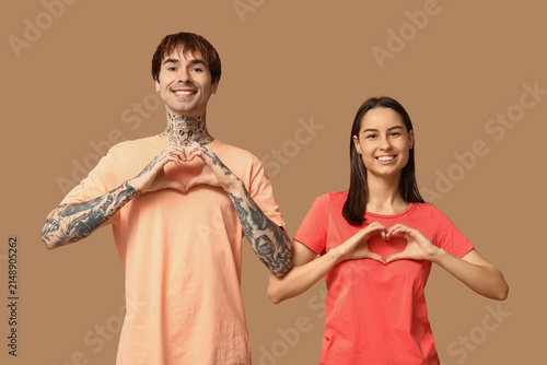 Young couple with making hearts with hands on beige background