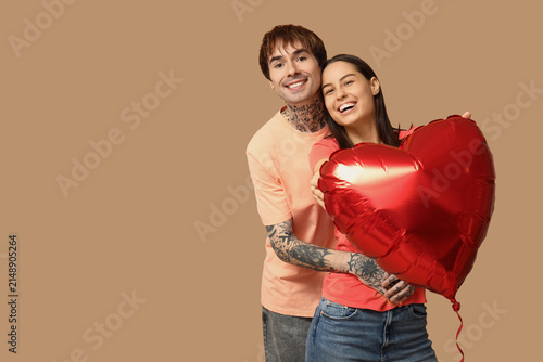 Young couple with heart-shaped air balloon on beige background