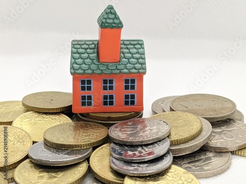 Miniature house model placed on assorted coins symbolizing real estate investment, property value, savings and financial planning.