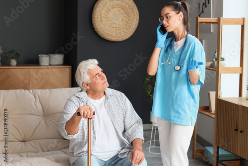 Senior man and nurse talking by mobile phone at home