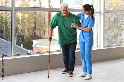 Nurse helping senior man with stick to walk at hospital