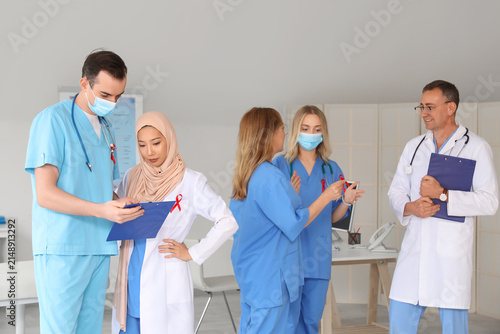 Professional team of doctors with red ribbons discussing something in clinic....