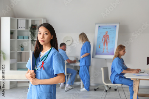 Young female doctor with red ribbon in clinic. World AIDS Day concept