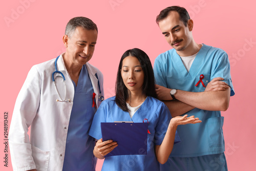 Professional team of doctors with red ribbons discussing something on pink ba...