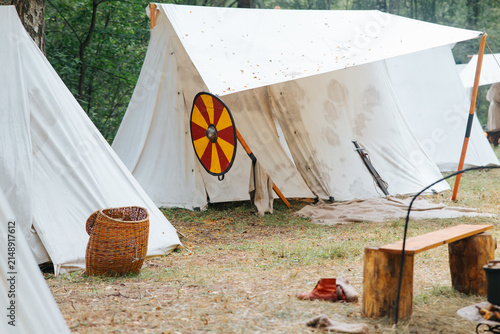 Obraz na plátně A medieval reenactment setting with white canvas tents and a brightly colored shield hanging
