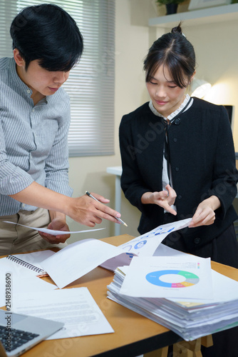 Analyzing Business Growth, Two professionals in a bright office setting, meticulously reviewing charts and graphs on documents