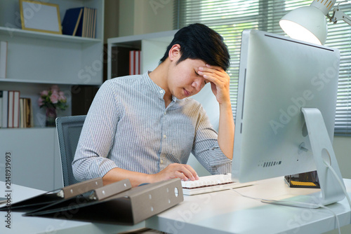 Stressed young professional man feeling overwhelmed while working remotely at his bright home office desk