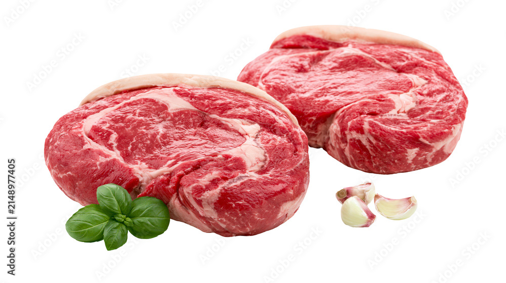 Obraz premium Two raw ribeye steaks with basil and garlic cloves