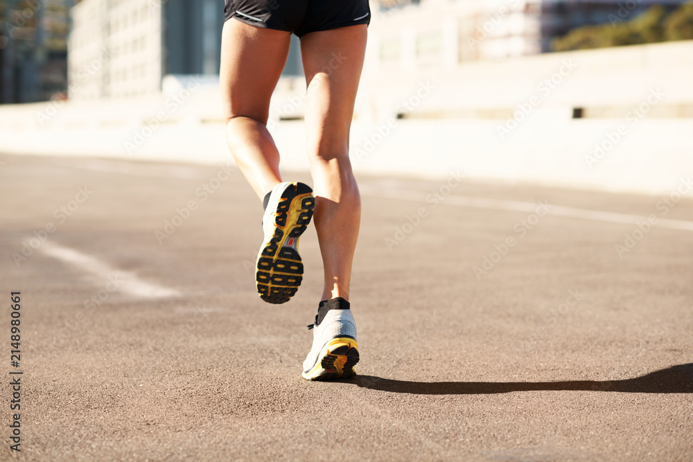 Obraz premium Fitness, active and legs in city with running, cardio and stamina exercise in physical activity. Training, space and female person outdoor with jog, sports hobby and athletic workout in town.