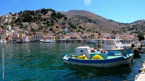 Colorful Greek island houses, old wooden fishing boats, crystal-clear blue sea, bright midday sun, calm water, Mediterranean harbor, cinematic, ultra-realistic.