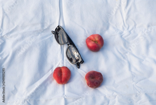 Fresh ripe peaches and sunglasses on a blanket outdoors, capturing a peaceful summer lifestyle.