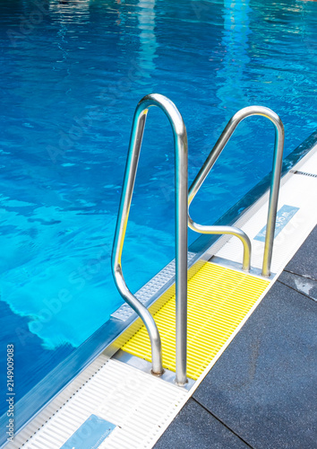Turquoise swimming pool water with stainless steel handrails on a sunny day.