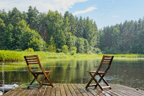 Foto two wooden chairs on pier by calm lake for relaxation and forest view