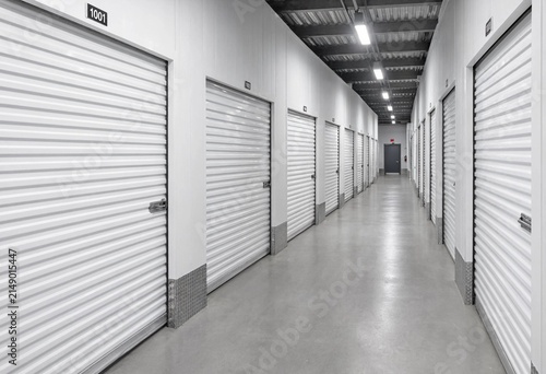 Modern self storage facility corridor featuring secure metal roll up doors, clean organized rental units, commercial warehouse interior, inventory management, and storage solutions.