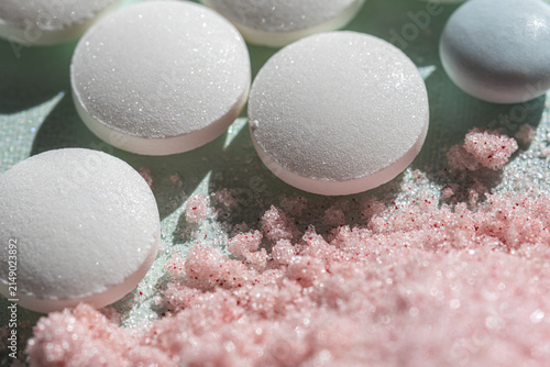 Several white round tablets rest on pink powder, combining smooth pharmaceutical forms with a contrasting textured surface. The image supports medication, healthcare and dosage concepts.
