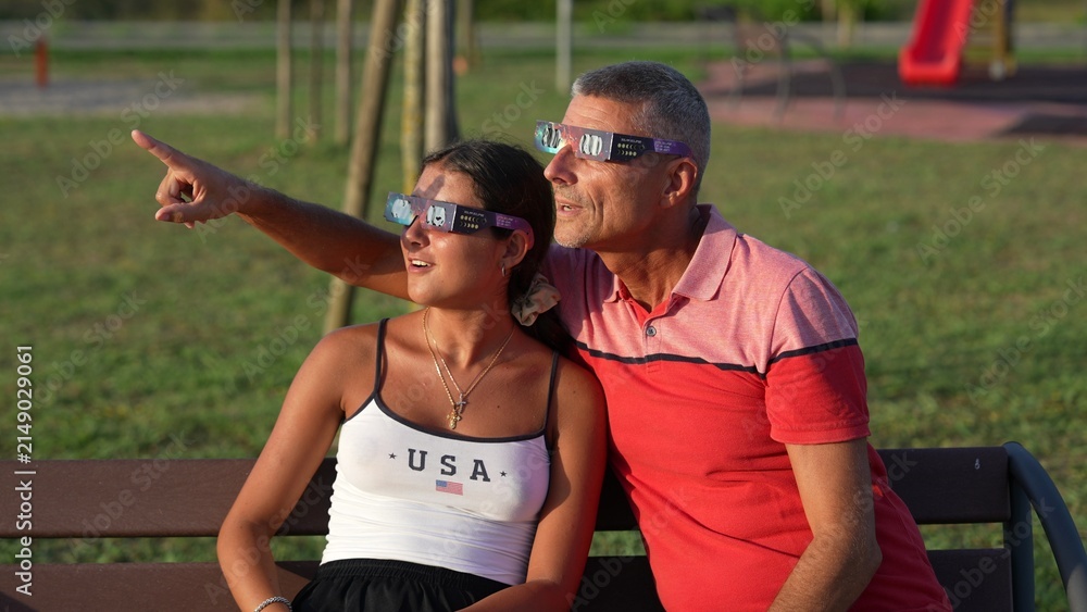 Obraz premium Man and daughter observing total solar eclipse with special protective glasses outdoors