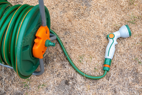 Foto Dried-up, sunburnt grass in garden due to the UK summertime hose pipe ban, with green hose pipe with grey watering nozzle laying on the ground