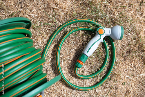 Foto Dried-up, sunburnt grass in garden due to the UK summertime hose pipe ban, with green hose pipe with grey watering nozzle laying on the ground