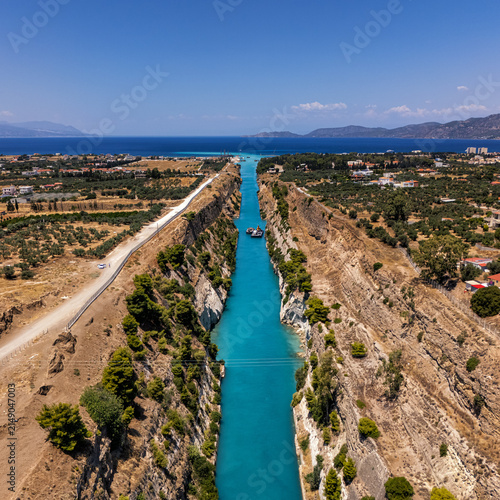 Aerial view of the Corinth Canal with its steep rocky walls and turquoise water, surrounded by olive groves and Mediterranean landscape in Greece.