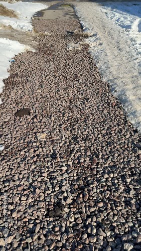 Close-up gravel path bordered by snow. Small stones and salt create gritty textured surface along pedestrian road during winter