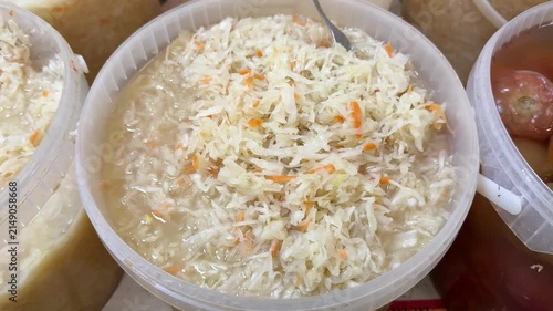 Fresh sauerkraut with carrot shreds displayed in transparent plastic container on market counter, market vendor presenting