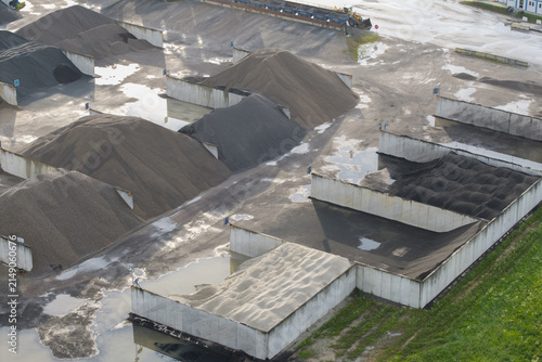 Aerial view of the bituminous mass plant featuring large piles of gravel and sand stored in concrete bays with puddles on the ground in Skawina, Lesser Poland Voivode, Poland.