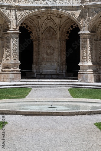 Lisboa, Lisboa, Portugal - 21 July 2026: View of Jeronimos Monastery featuring ornate Manueline stone arches, a central circular fountain, and manicured green lawns in the cloister courtyard.
