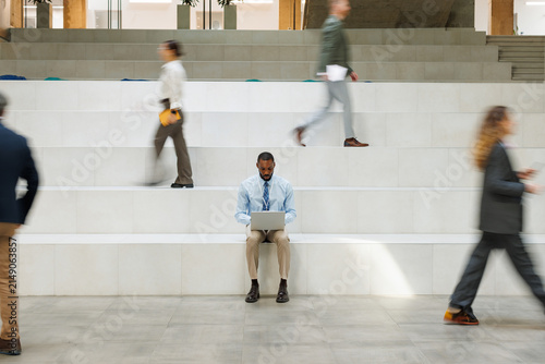 Focused businessman uses laptop on office stairs amidst rush