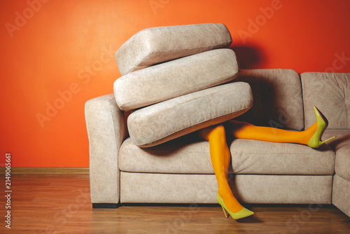 Woman in yellow tights buried by sofa cushions in bright surreal living room