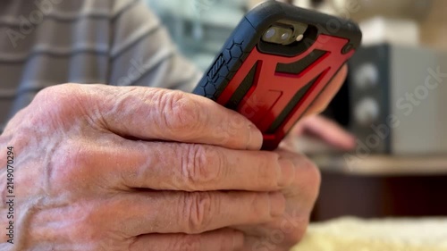 Elderly hands holding smartphone close-up, reading news on screen, large veins and wrinkled skin in sharp detail, sitting