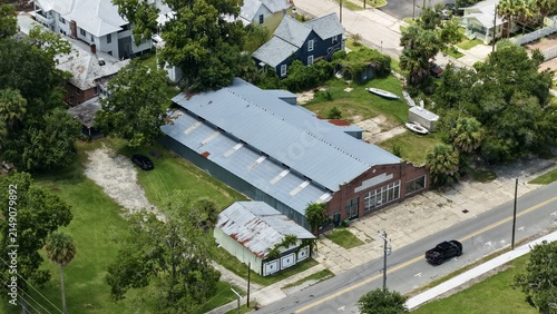 Aerial view of a long industrial building with a metal roof and brick facade, situated near a smaller outbuilding, surrounded by lush trees and green lawns in Palatka, Florida, United States.