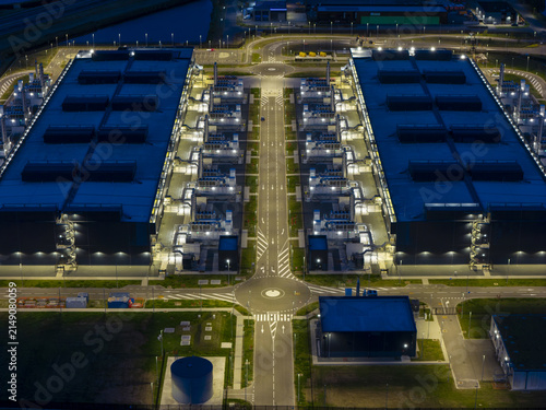 Aerial view of a large illuminated data center complex at night featuring symmetrical buildings, cooling infrastructure, and a central roundabout in Middenmeer, North Holland, Netherlands.