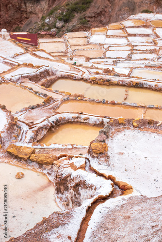 View of the historic Maras Salt Mines with terraced salt evaporation ponds, stone walls, and mineral-rich water in Cusco, Cusco, Peru.