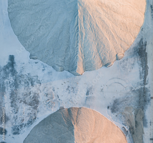 Aerial view of two symmetrical sea salt stockpiles divided by a textured mineral surface, illuminated by soft golden sunset light in France.