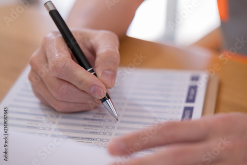 Konstfotografi Person completing a questionnaire with pen on paper, representing survey, assessment, feedback, evaluation, checklist, research, data collection and customer satisfaction in a professional setting