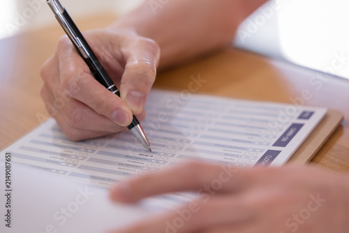 Quadro su tela Person completing a questionnaire with pen on paper, representing survey, assessment, feedback, evaluation, checklist, research, data collection and customer satisfaction in a professional setting