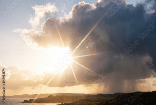 Dramatic sunburst breaks through storm clouds above a rugged coastline