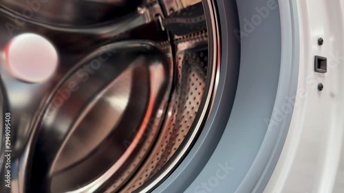 Close-up steel drum washing machine door showing gleaming stainless interior with perforated pattern, open rubber gasket, visible.