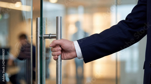 Professional man's hand opening a sleek, modern glass door with a contemporary stainless steel handle.
