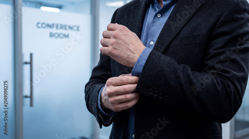Businessman adjusts his sleeve cuff before entering a conference room.