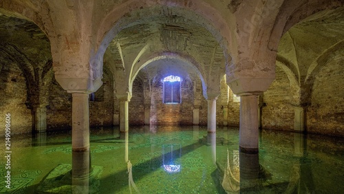View of the flooded crypt of the Basilica of Saint Francis with ancient stone columns and arches reflecting in the clear water in Ravenna, Emilia-Romagna, Italy.
