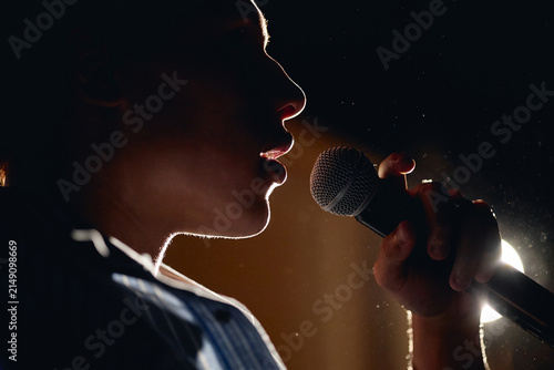 Foto Silhouette of teenager singing into microphone on stage during student theater performance