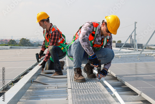Engineer inspecting solar panel installation on industrial roof Technician in safety vest checking commercial rooftop solar array. Professional worker monitoring green energy solar panels on roof.
