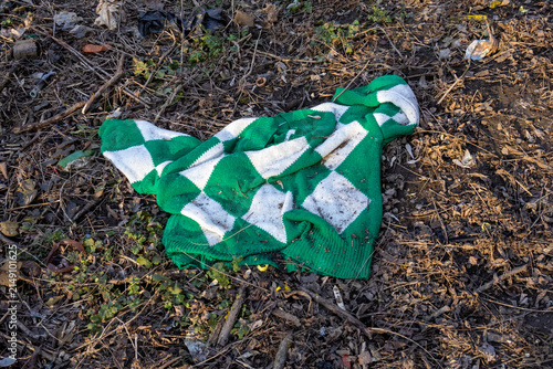 Fotografie Discarded green and white sweater lying as trash on ground stock photo